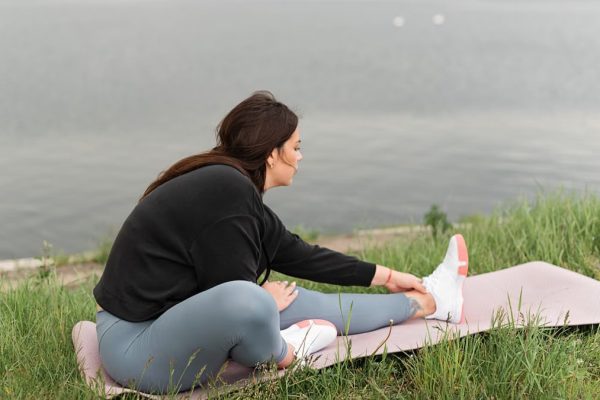 A woman stretches on a yoga mat by a serene lake, embodying relaxation and wellness in nature.
